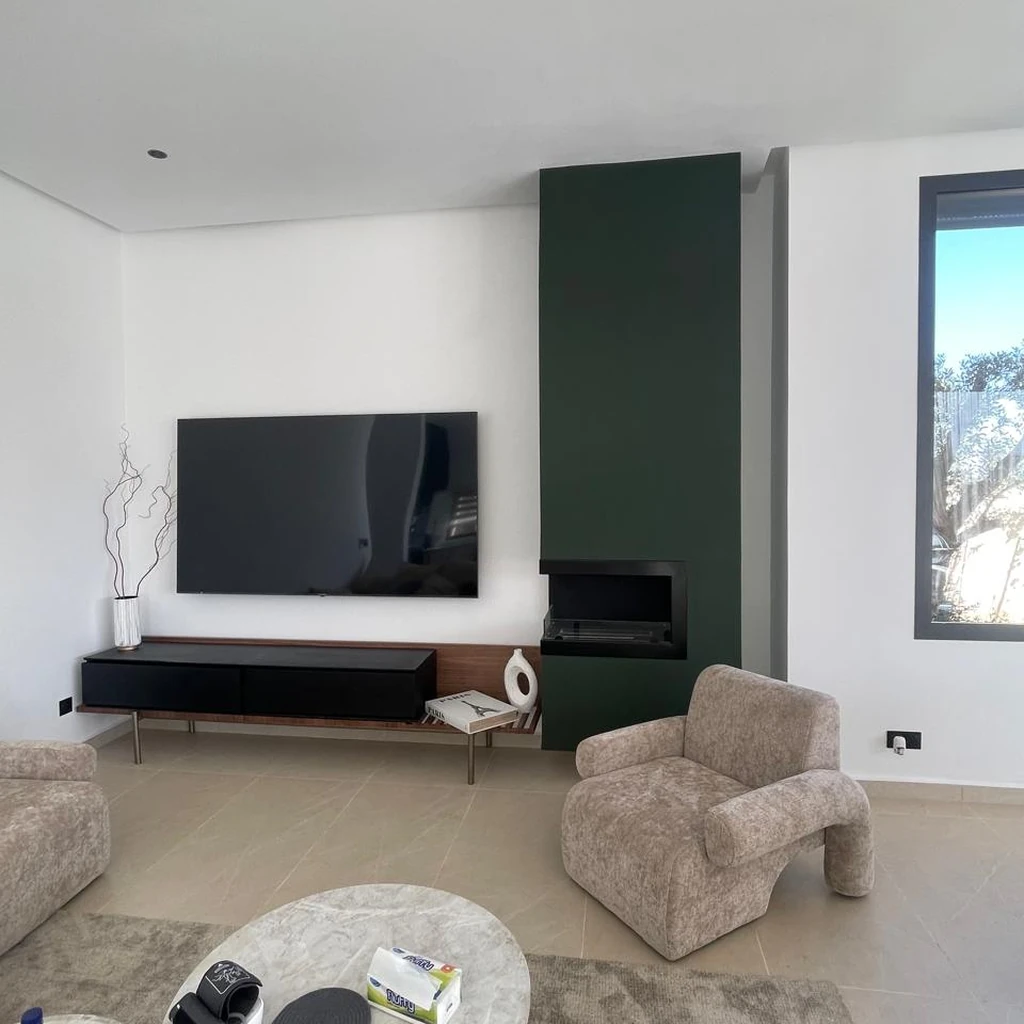 Cheminée contemporaine encastrée dans un habillage vert foncé au sein d’un salon moderne.
